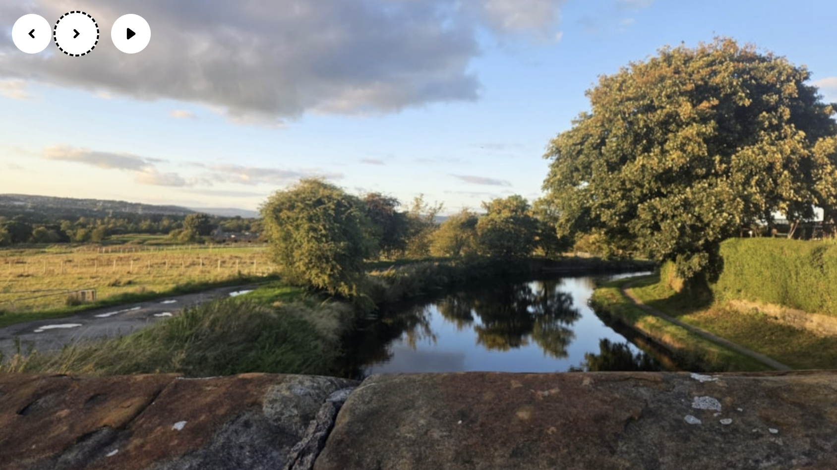A photo of countryside overlaid with a left, right and play button. The right button has a dotted line around it.